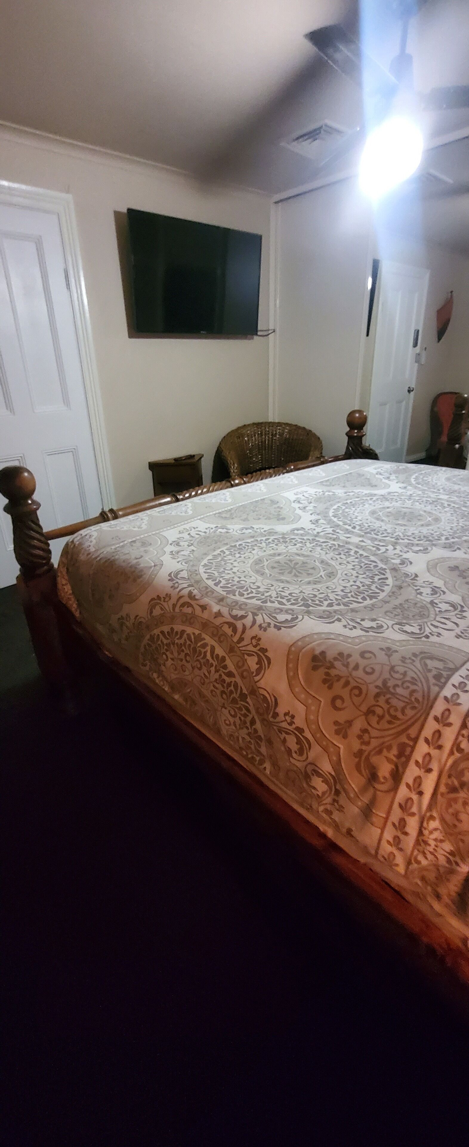 Een slaapkamer met een groot bed, een aan de muur bevestigde televisie, een deur en een stoel.