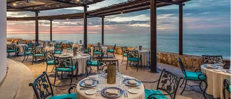 An outdoor dining area with tables set for two, overlooking the sea.