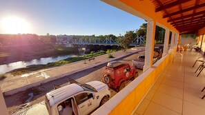 A view from a balcony overlooking a river, a bridge, and a parking area with a white van and a red vehicle. - POUSADA BEIRA RIO - JALAPÃO (Ponte Alta do Tocantins)