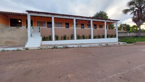 A two-story building with a white exterior and orange walls, featuring a covered porch with steps leading to the entrance. - POUSADA BEIRA RIO - JALAPÃO (Ponte Alta do Tocantins)