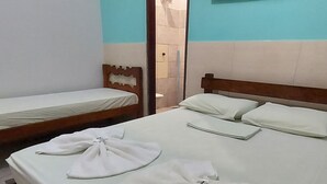 A hotel room with a large bed, two smaller beds, a TV, and a bathroom visible through an open door. - POUSADA BEIRA RIO - JALAPÃO (Ponte Alta do Tocantins)