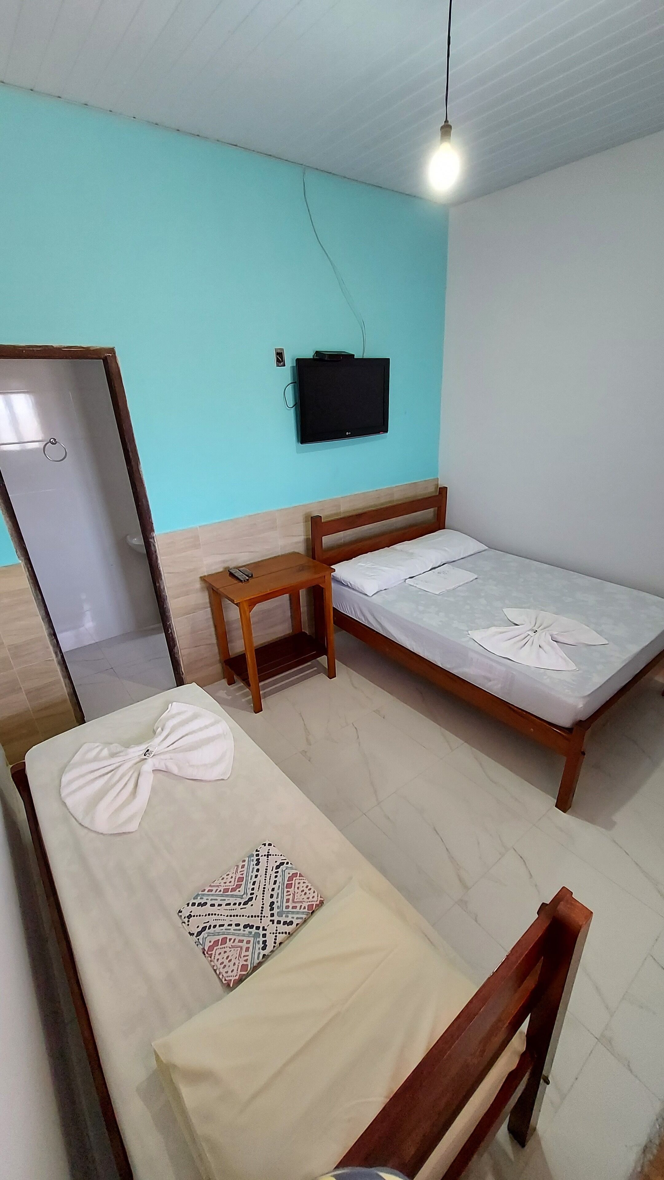 A small, simple room with a bed, a wooden table, a TV mounted on the wall, and a door.