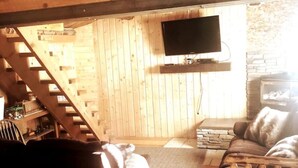 L’intérieur chaleureux d’un chalet avec un escalier en bois, un téléviseur à écran plat fixé au mur, une cheminée et un coin salon confortable comprenant un canapé et un fauteuil.