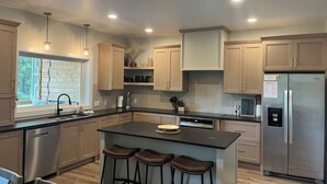 A modern kitchen with wooden cabinets, a stainless steel refrigerator, and a large window.
