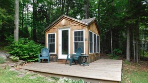 A wooden cabin with a deck, two chairs, and a table.