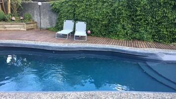 Una piscina con dos sillas reclinables blancas y una siega en el fondo.