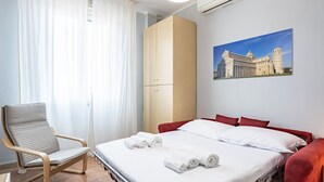 Ein Hotelzimmer mit einem Bett, einem Sessel, einem Kleiderschrank und einem Gemälde an der Wand.