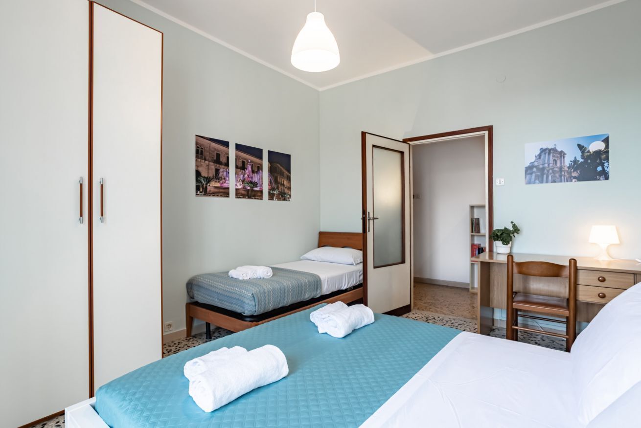 A hotel room with two beds, a desk, a chair, a wardrobe, and a mirror.