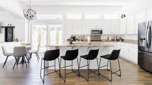 A modern kitchen with white cabinets, a large island with bar stools, a built-in microwave, and a stainless steel refrigerator. - Gorgeous Lakefront Home with Infinity Pool & Hot Tub, Sleeps Up to 12 (Glendale)