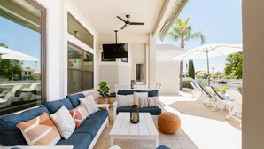 A sunlit outdoor seating area with a sofa, white coffee table, and lounge chairs. - Gorgeous Lakefront Home with Infinity Pool & Hot Tub, Sleeps Up to 12 (Glendale)