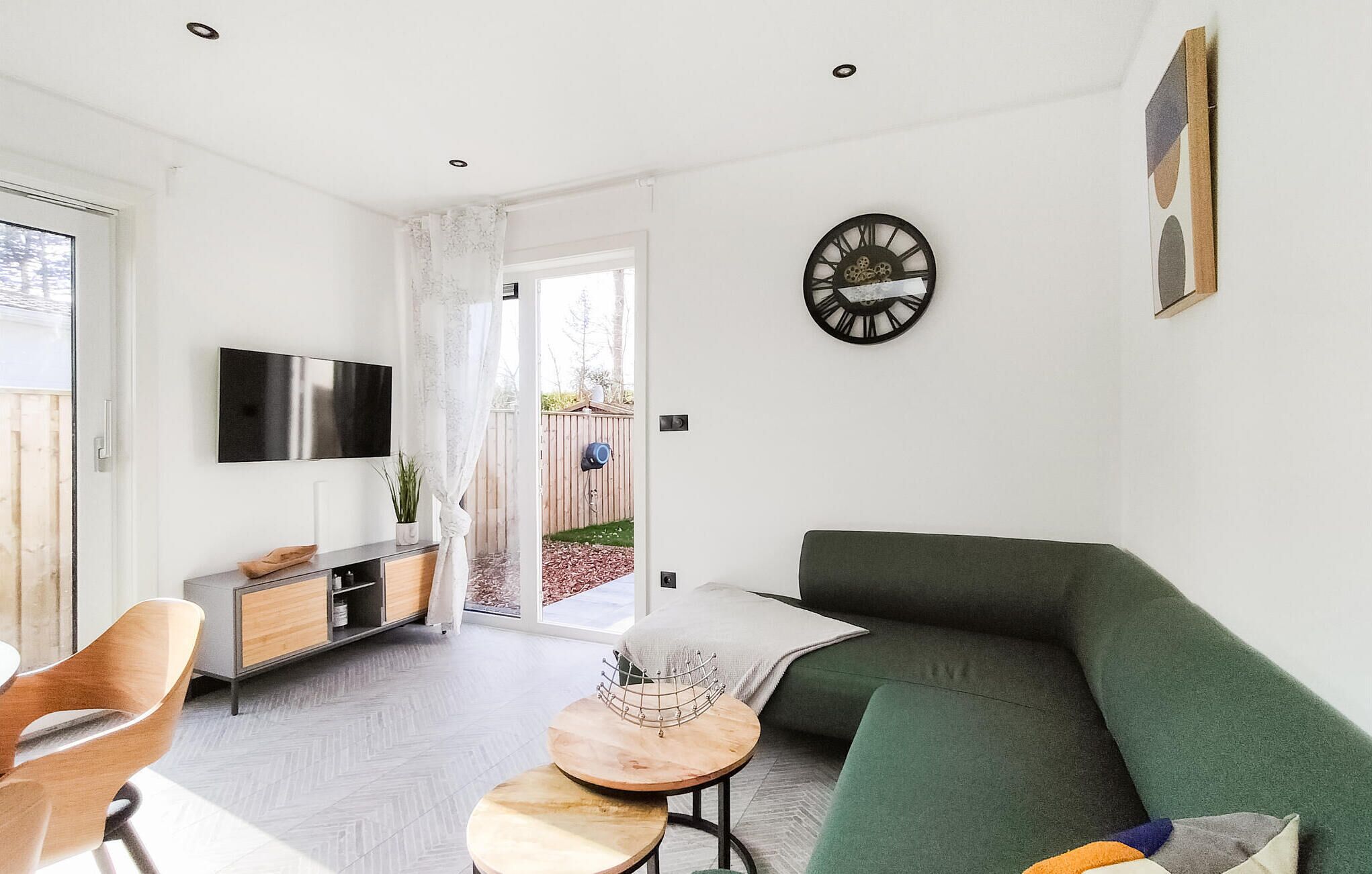 Een moderne woonkamer met een groene bank, een houten salontafel en een aan de muur bevestigde televisie.