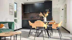 Een knus woongedeelte met een eethoek, kitchenette en een groene bank.
