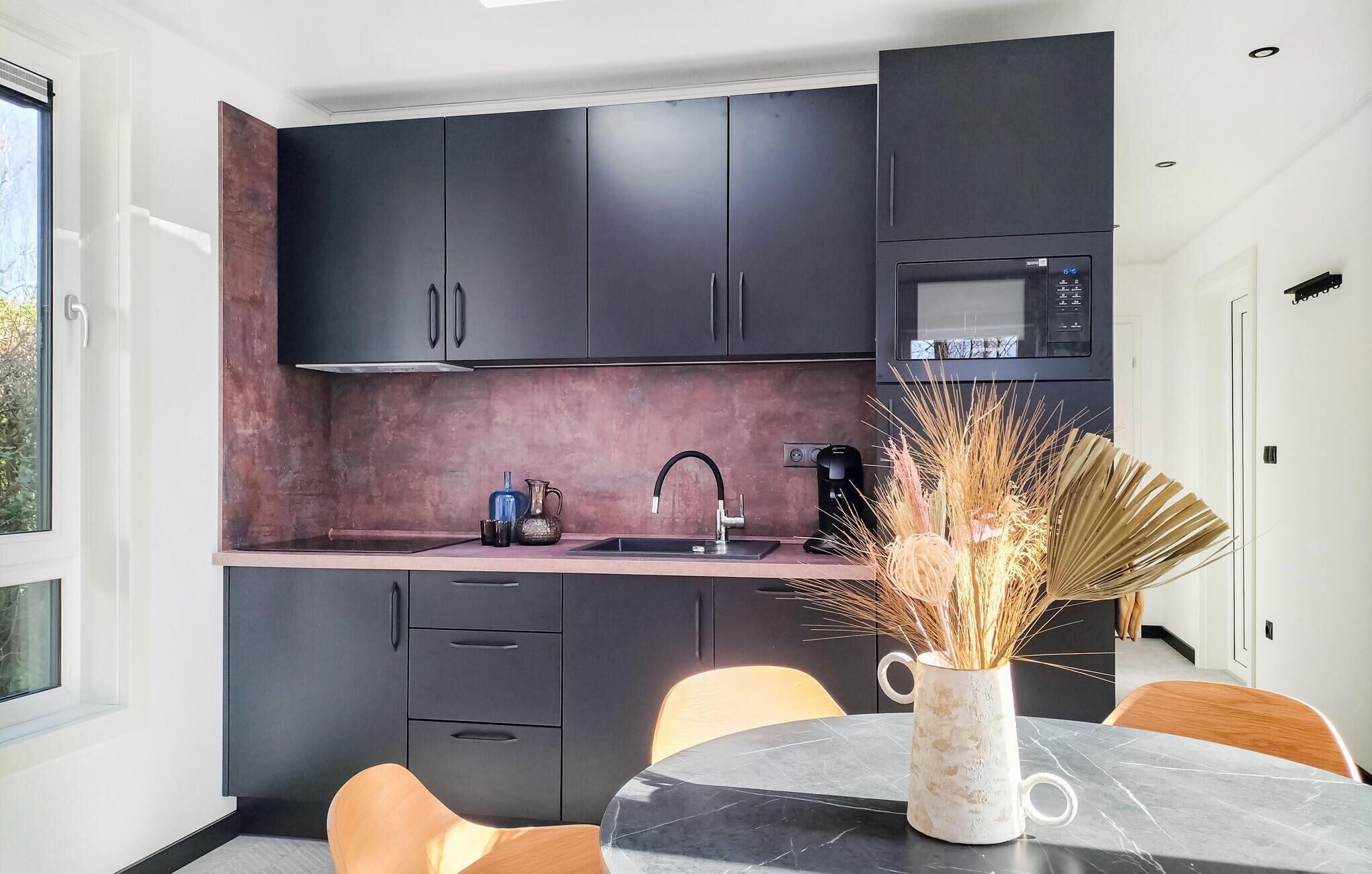 A modern kitchen with dark cabinets, a microwave, a sink, and a dining area with a table and chairs.