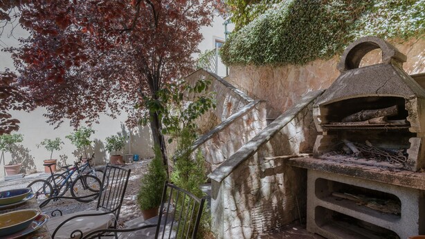 Un horno de piedra, asientos al aire libre y plantas en macetas en un patio.