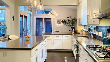 Cocina moderna con armarios blancos, una isla grande, luces colgantes y vistas al exterior.