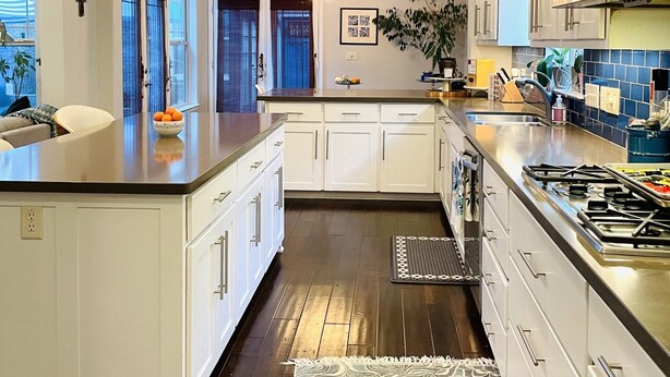 A modern kitchen with white cabinets, a large island, pendant lights, and a view to the outside.