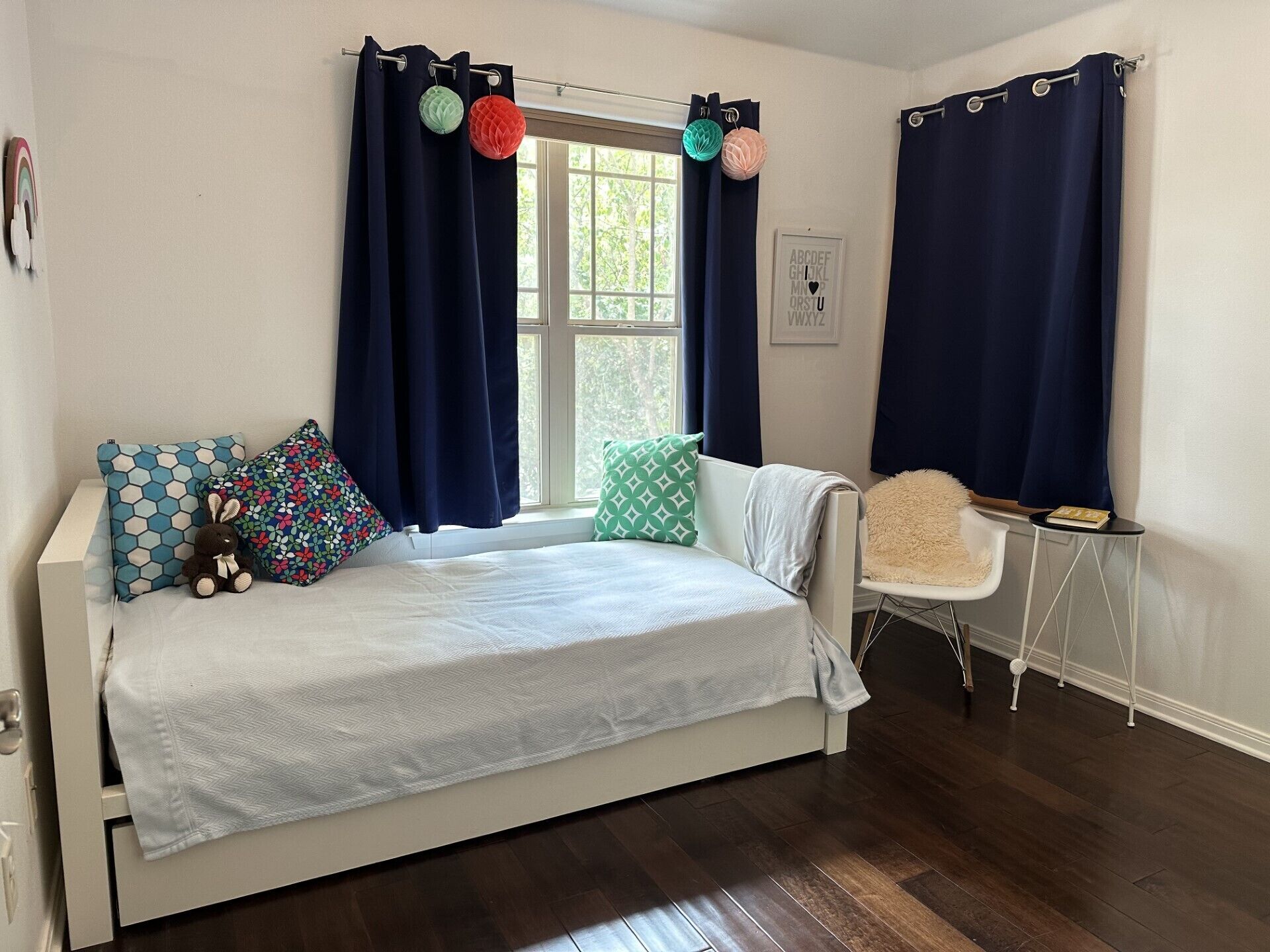 A bedroom with a bed, a chair, a window with curtains, and a small table.