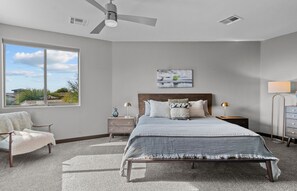 A bedroom with a large bed, a chair, a nightstand, a lamp, and a ceiling fan.