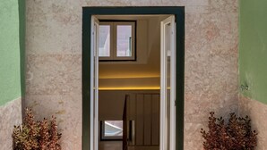 Een interieurzicht van een gang met een deur die naar een kamer leidt. De gang heeft een gestructureerde wand en een deurkozijn in het groen. Aan beide zijden van de deur staan twee kleine planten.