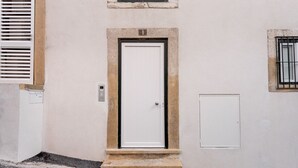 Eine weiße Tür mit einem kleinen Fenster darüber, eine weiße Stromkasten rechts daneben und ein Betonfundament.