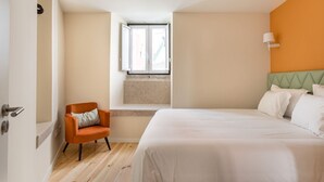 Ein Hotelzimmer mit Bett, Fenster, Stuhl und einer Wandlampe.
