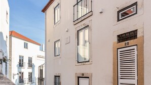 Une rue étroite bordée d’immeubles dotés de balcons, d’un toit en tuiles et d’une porte blanche avec des volets.