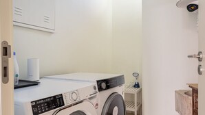 Een wasruimte met een voorlader wasmachine en droger, een klein tafeltje met een handdoek, en een wastafel met een marmeren aanrecht.