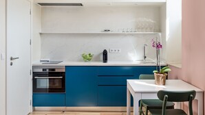 A compact kitchen with a white countertop, blue cabinets, a small oven, and a dining area with a white table and chairs.