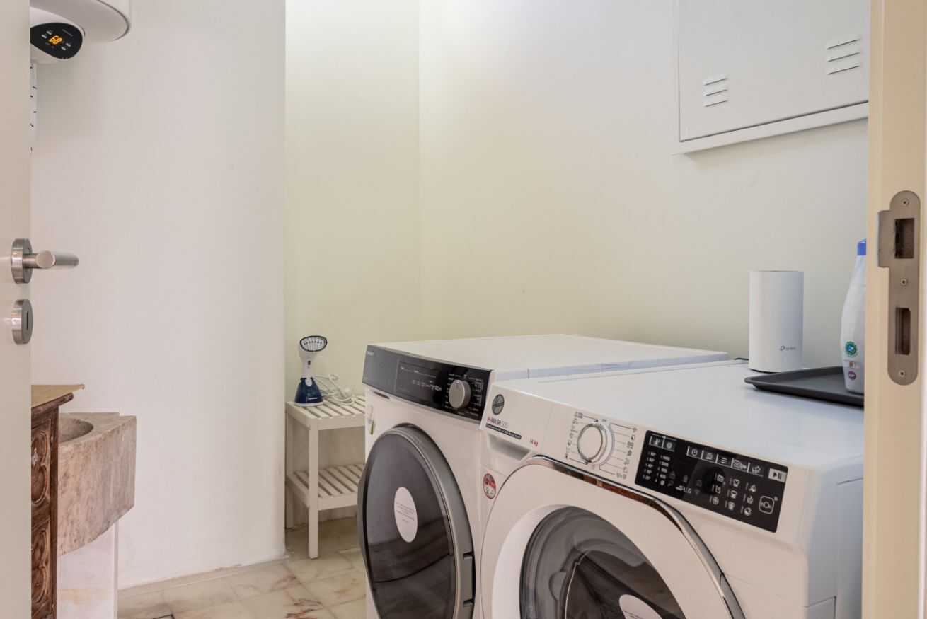 A laundry room with two front-loading washing machines, a small shelf with a glass container, and a white wall-mounted heater.