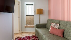 A living room with a green sofa, a flat-screen TV, a lamp, and a window with a view. - JOIVY Modern apt near Rossio Square (Lisboa)