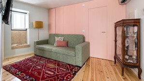 A room with a green sofa, a patterned red rug, a wooden cabinet, and a pink wall. - JOIVY Modern apt near Rossio Square (Lisboa)