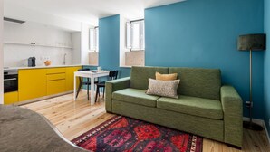 Un espace de vie compact avec un canapé vert, un tapis à motifs et une cuisine jaune.