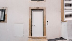 Une ruelle étroite avec une porte blanche, une petite fenêtre ornée de barreaux en métal et une boîte électrique blanche fixée au mur.