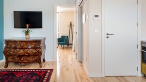 Un couloir doté d’un plancher en bois, d’un tapis à motifs rouges, d’une commode en bois avec des tiroirs, d’un téléviseur fixé au mur et d’une porte avec une poignée.