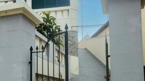 Une entrée fermée par un portail, avec un escalier menant à un bâtiment doté d’une façade en pierre et d’une fenêtre verte.
