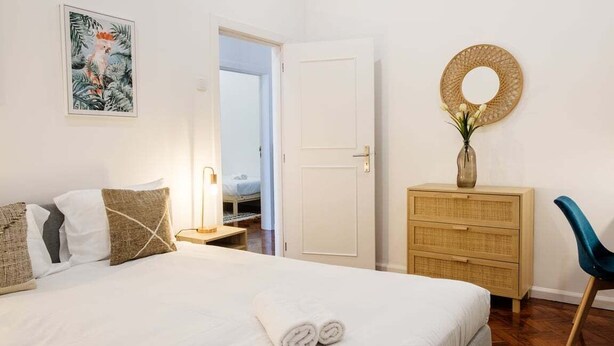 Une chambre à coucher comprenant un lit, une table de chevet, une commode, une chaise et une porte donnant sur une autre pièce.