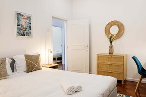 A bedroom with a bed, bedside table, dresser, chair, and a door leading to another room. - GuestReady - Blissful Getaway in Funchal (Funchal)