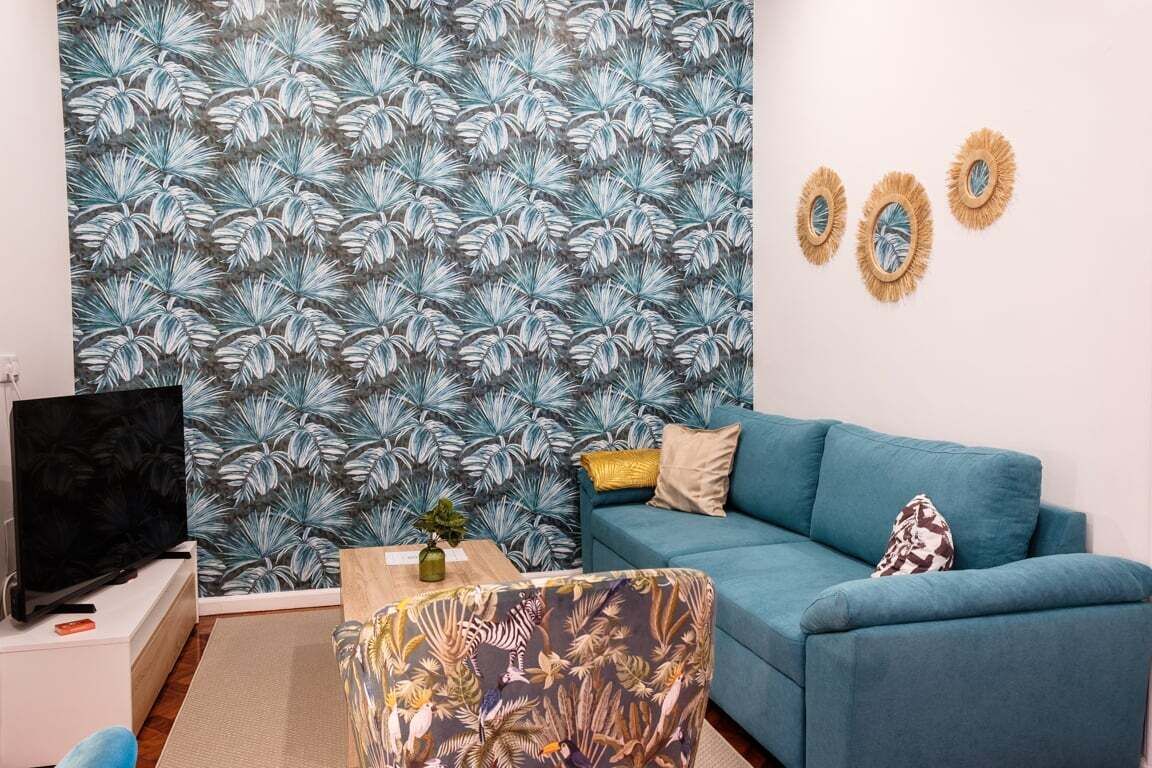 Un soggiorno con un divano blu, una televisione e una parete decorata.