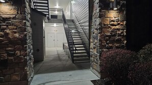 Um corredor estreito com paredes de pedra e escada de metal que dá para um segundo andar.