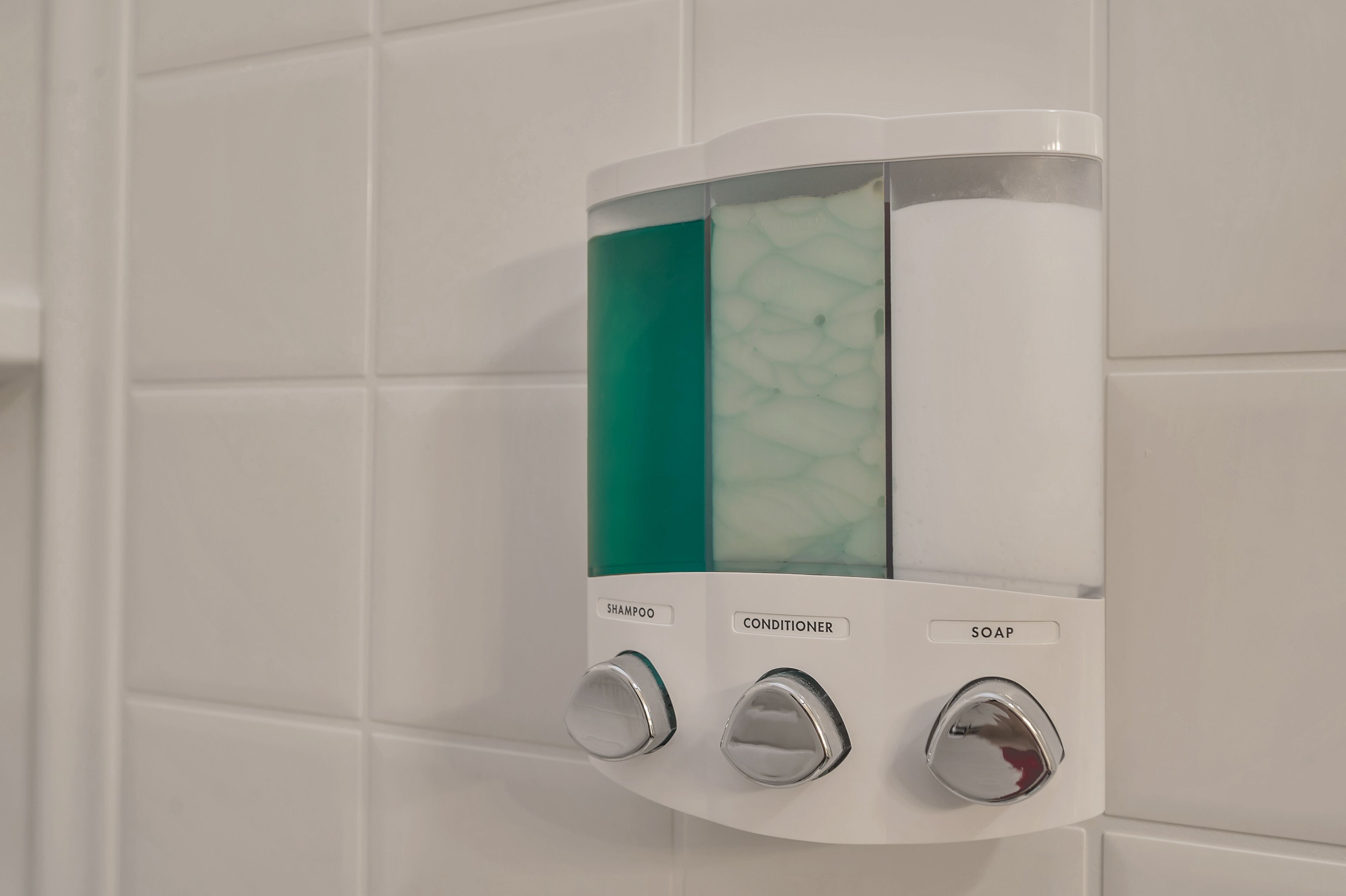 Eine wandmontierte Spenderstation mit getrennten Fächern für Shampoo, Conditioner und Seife.