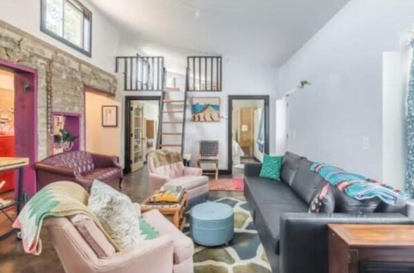 Amplia sala de estar con un sofá grande, sillones y una mesa de centro. Se ve una escalera que sube a un nivel superior, y una puerta que da a otra habitación.