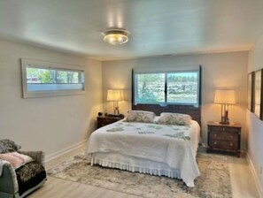 Un dormitorio con cama, dos mesitas de noche con lámparas, una ventana con vistas y una silla.