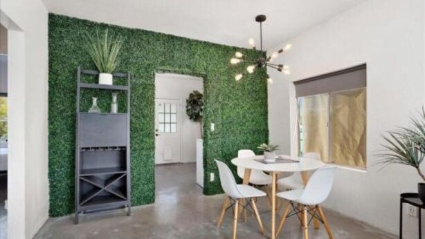 Een moderne eetruimte met een groene wand, witte stoelen en een kroonluchter.