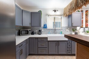 A modern kitchen with grey cabinets, a stainless steel refrigerator, a microwave, a coffee maker, and a sink.