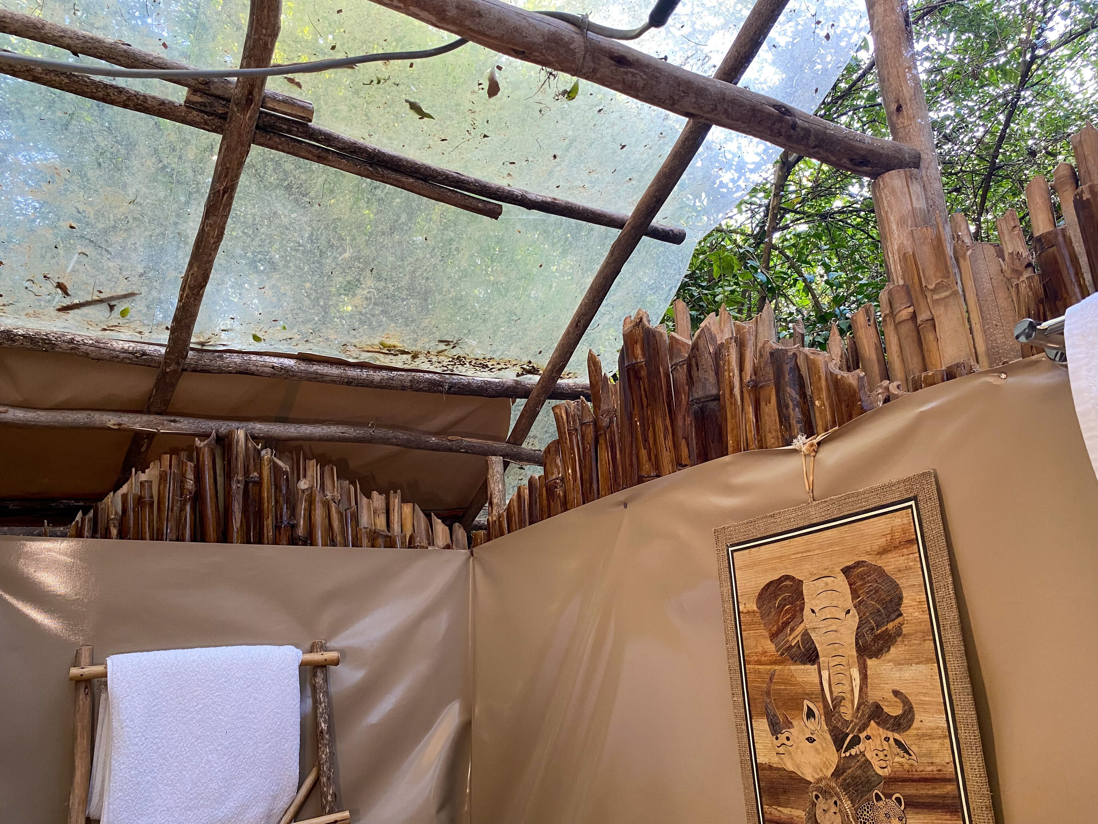 A rustic wooden structure with a transparent roof, a white towel hanging, and a framed artwork on the wall.