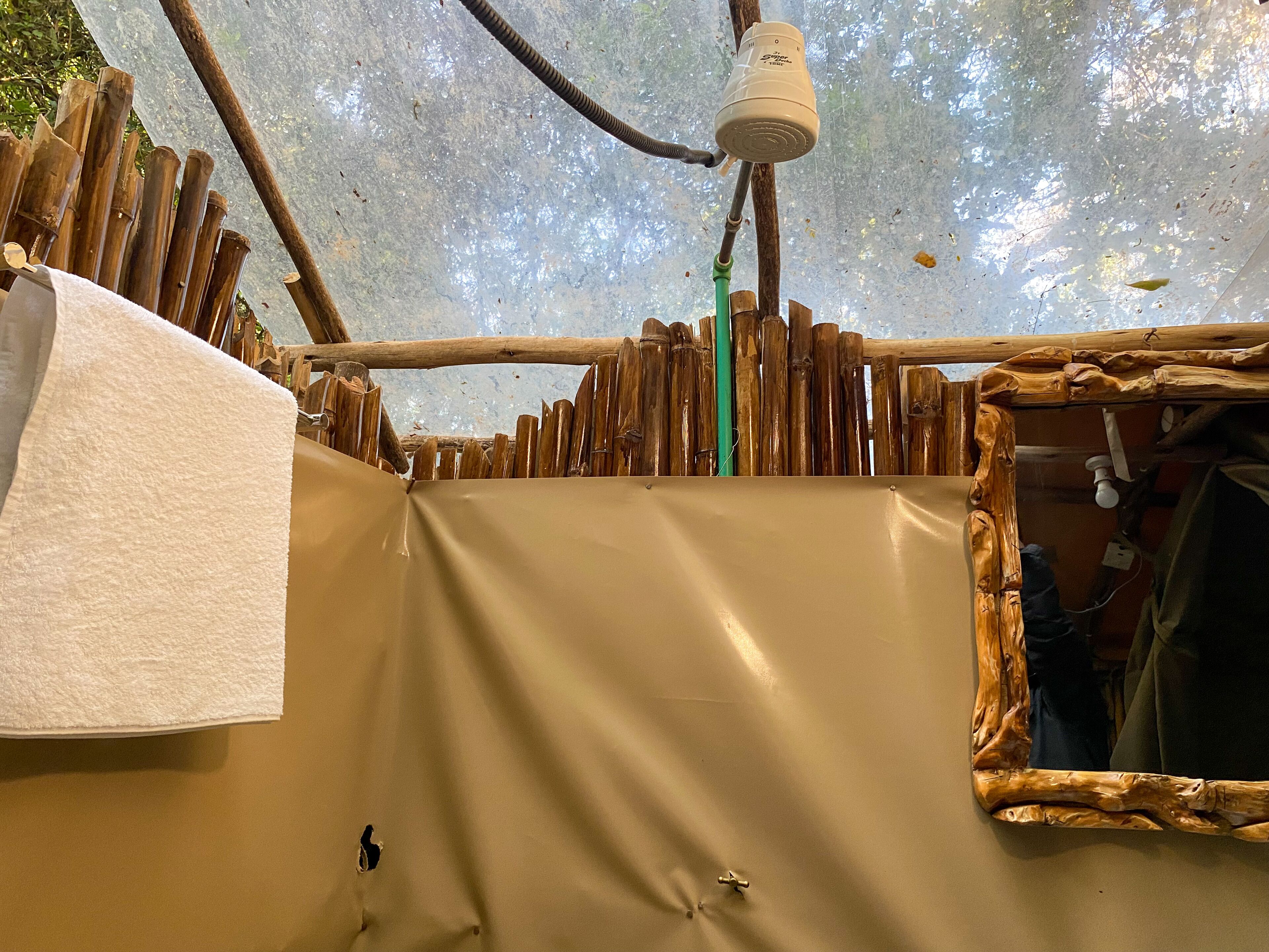 A tent-like structure with a tarp floor, wooden poles, and a hanging water container.