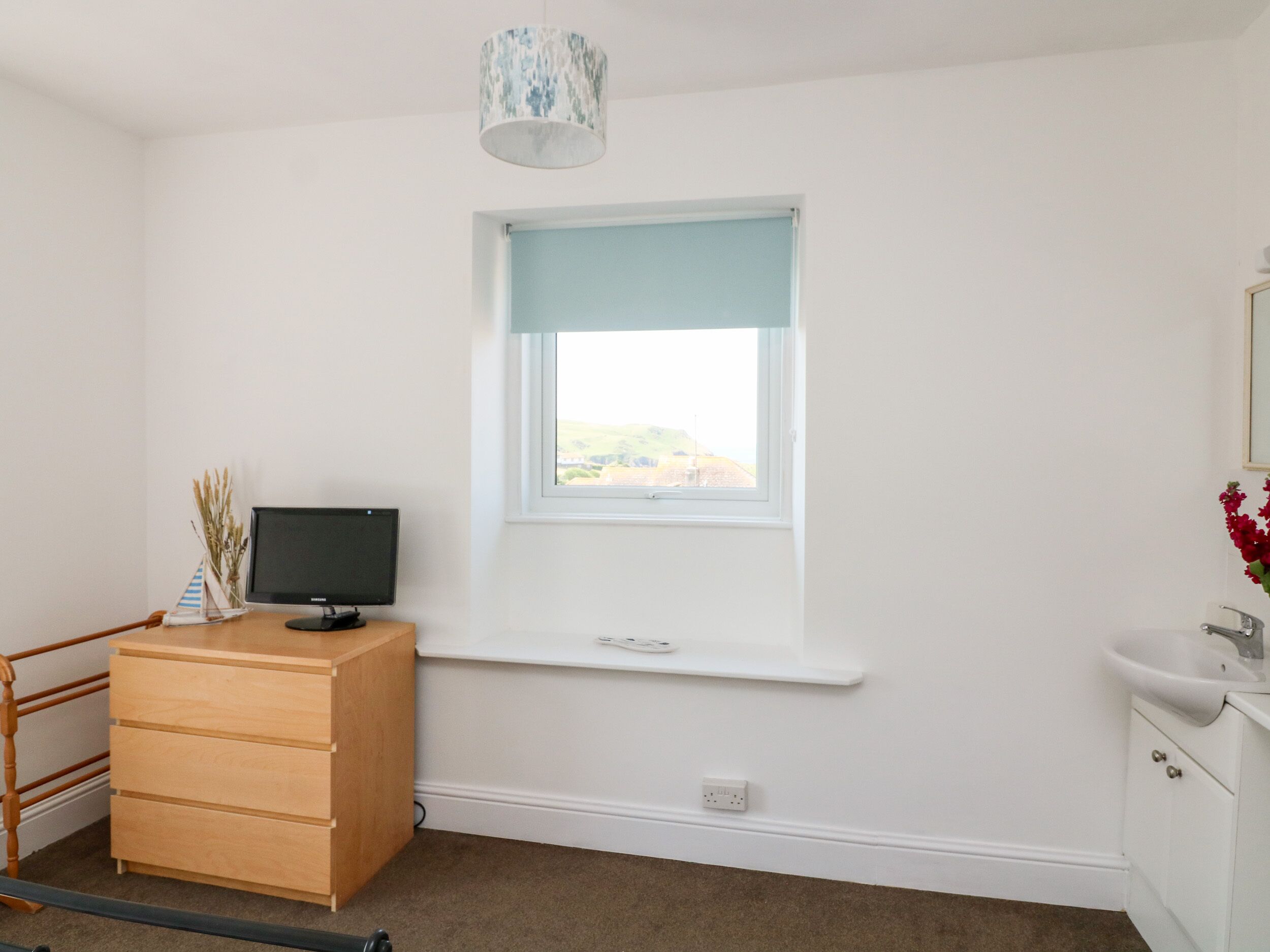 A room with a desk, a computer, a window with a view, a small shelf, and a white cabinet.