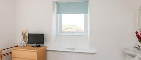 Una habitación con escritorio, computadora, ventana con vistas, estante pequeño y armario blanco.