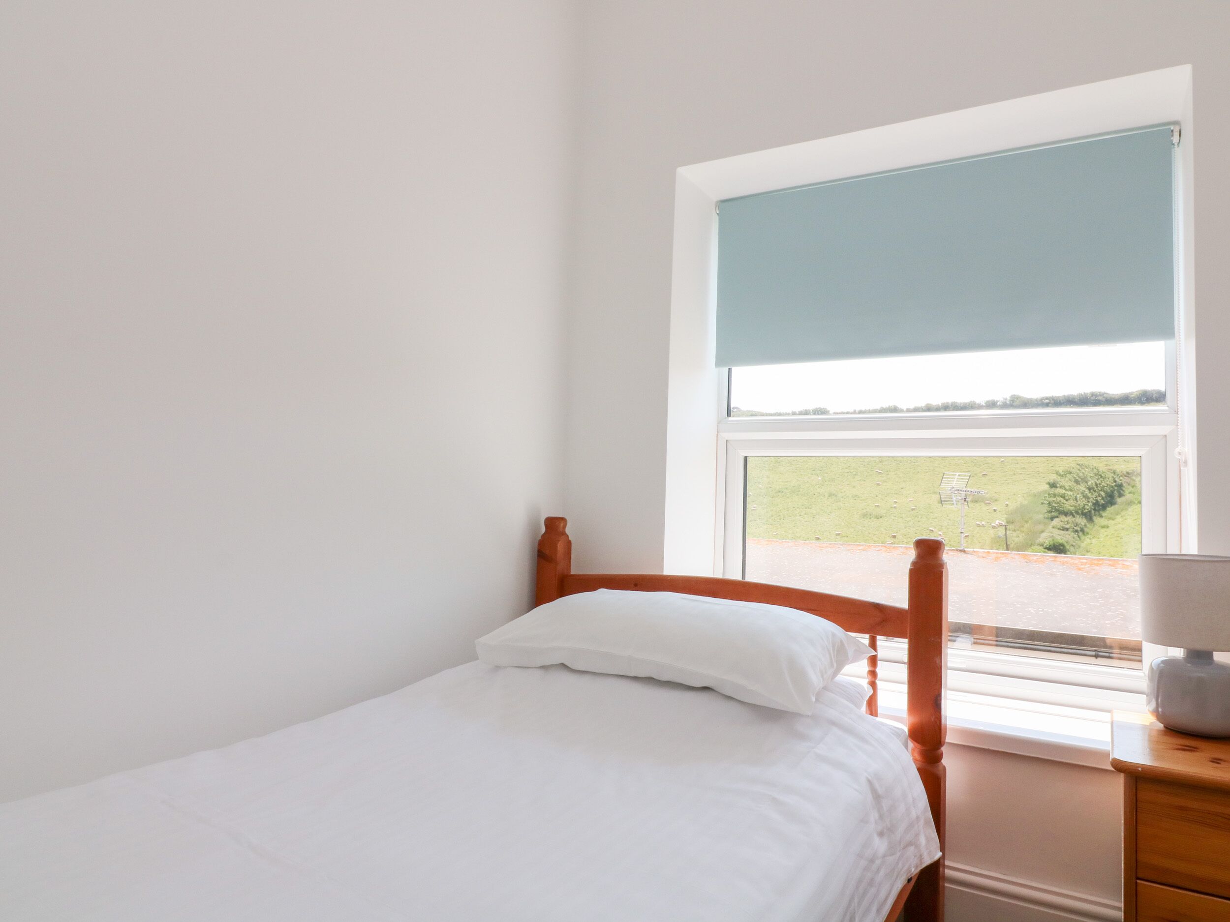 A single bed with white bedding in a room with a window.