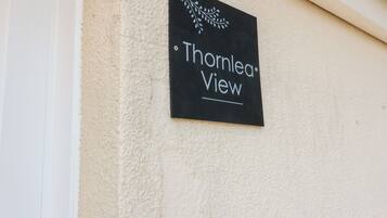 En svart skylt med vit text som visar "Thomlea View", placerad på en vägg med en mönstrad, beige yta.